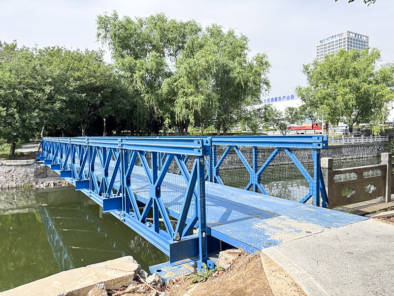 24 metrů dlouhý, modře lakovaný antikorozní, jednořadý jednovrstvý vyztužený most pro pěší Bailey